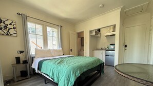 A bedroom with a bed, a desk, a chair, a small kitchenette, and a bathroom. - Comfortable Studio Unit on 2nd Floor (Los Angeles)