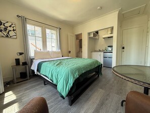 Ein Schlafzimmer mit Bett, Schreibtisch, Stuhl, einer kleinen Küchenzeile und einem Badezimmer.