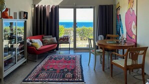 Un salon avec un canapé rouge, une vitrine, une table à manger avec des chaises et une vue sur l’océan.