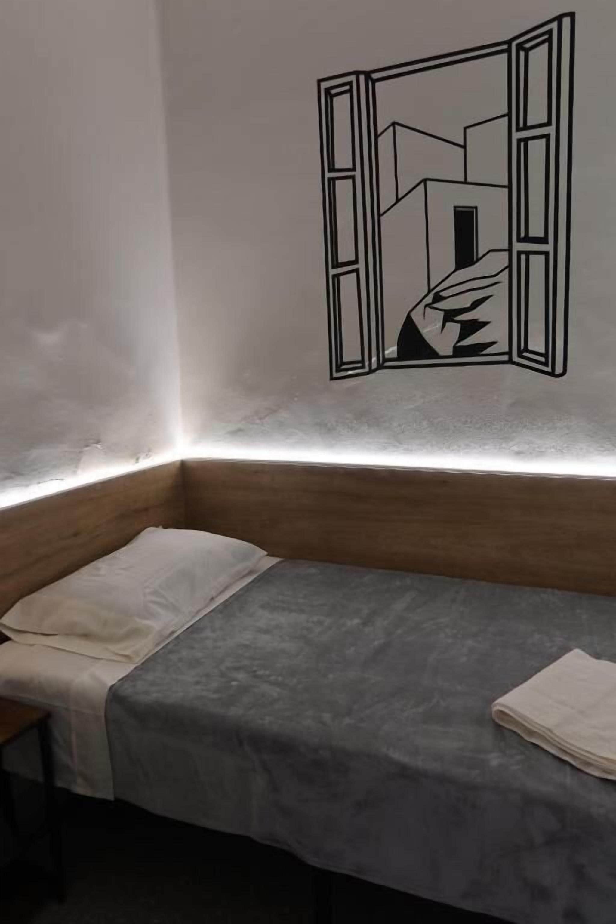 A room with a bed, a window with a geometric wall decal, and a wooden bench.