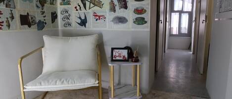Una habitación con un sofá blanco, una mesita con un marco de fotos y una pared decorada con varias ilustraciones.