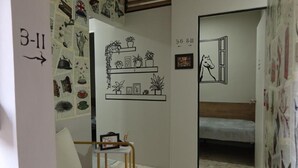 Una habitación con una litera, una silla, una pared con estantes de plantas y una puerta con ventanal.