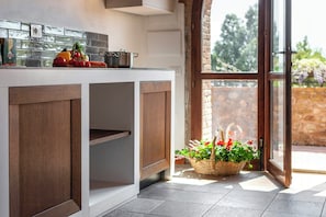 A kitchen with a white countertop, wooden cabinets, and a basket of flowers near a glass door. - Apartment in farmhouse with terrace in Maremma (Massa Marittima)