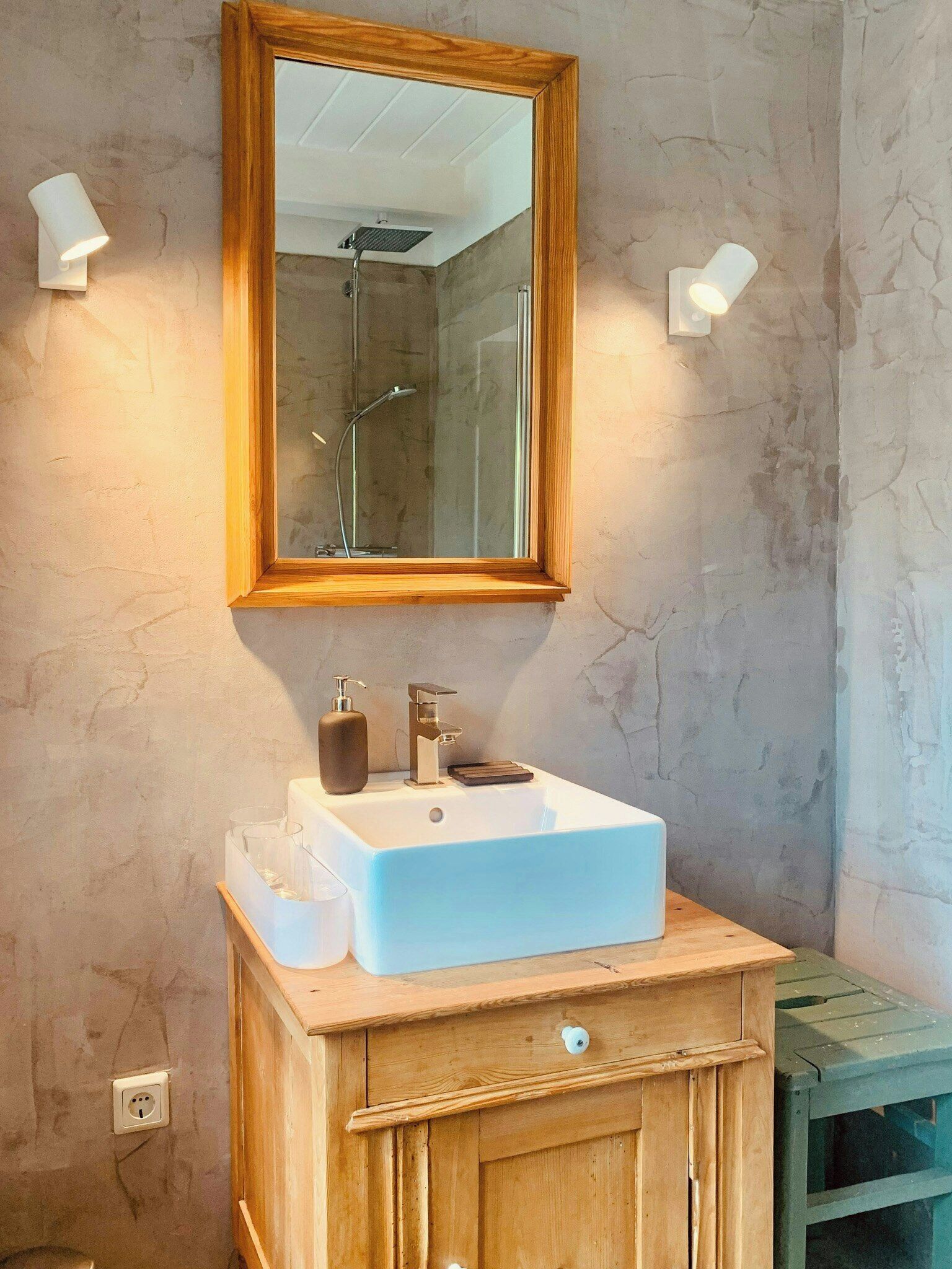 Une salle de bain avec un meuble-lavabo en bois, un lavabo blanc, un miroir et deux appliques murales.