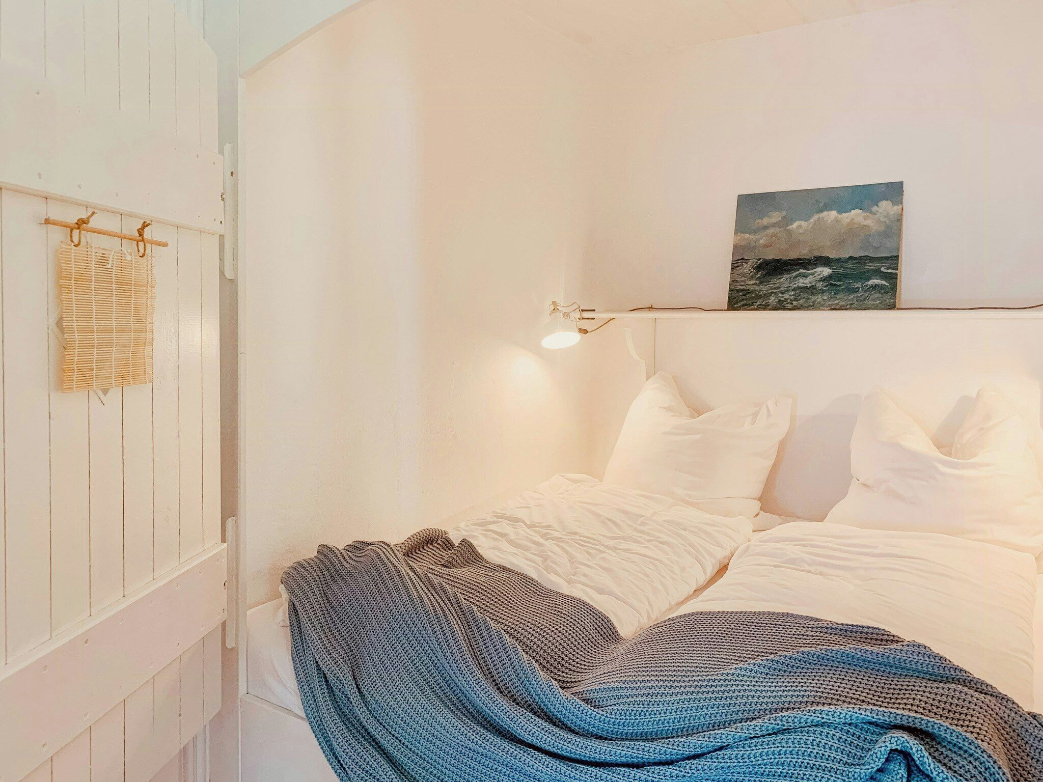 Un dormitorio con cama, paredes blancas, un cuadro y una ventana con persianas.