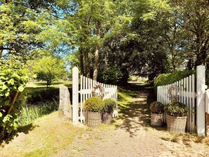 Ein Weg, der durch einen Garten mit weißem Zaun, Steinpfeilern und Kübelpflanzen führt.