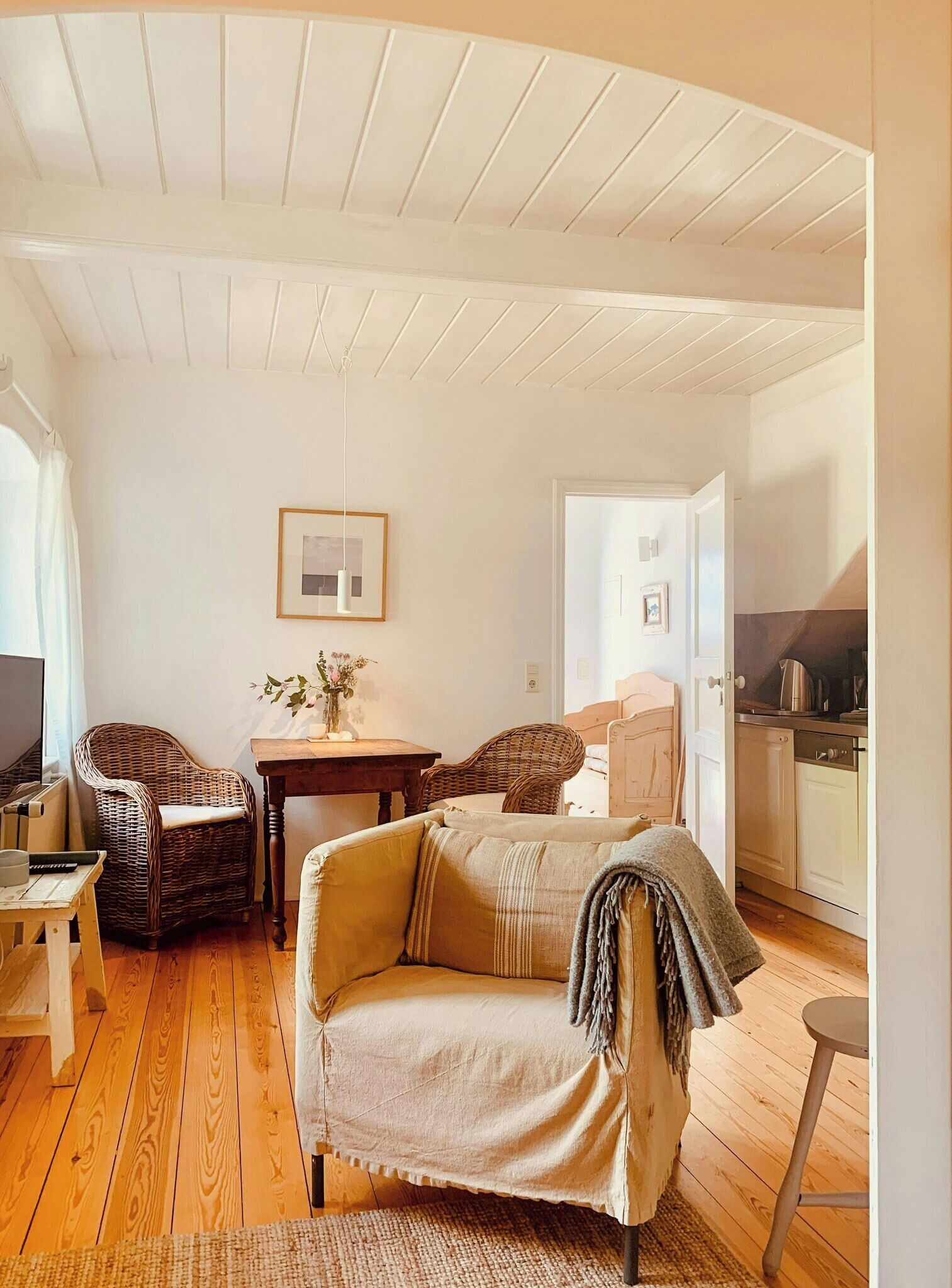 A cozy living room with a sofa, chairs, a table, and a kitchen area in the background.