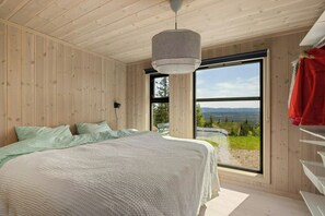 A bedroom with a large bed, a hanging light fixture, and a window with a view of the outdoors.