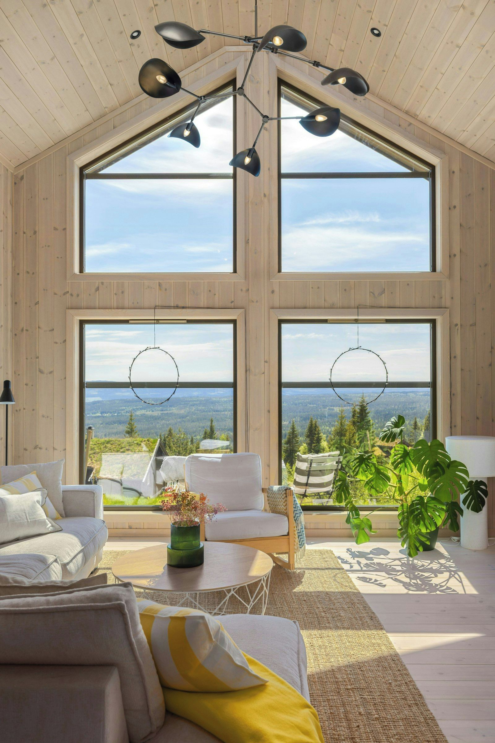 A spacious room with a high ceiling, large windows, and a view of a forested landscape.