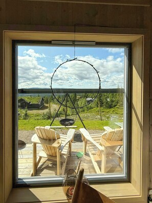 A room with a large window overlooking a deck with wooden chairs and a hanging fire pit. - Modern cabin with ski-in/out near Birken trails (Rena)