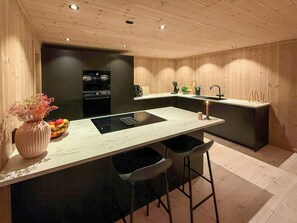 A modern kitchen with a central island, bar stools, a built-in oven, and a sink. - Modern cabin with ski-in/out near Birken trails (Rena)