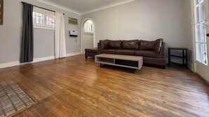 Ein geräumiges Wohnzimmer mit Holzböden, einem braunen Ledersofa und einer Deckenleuchte.