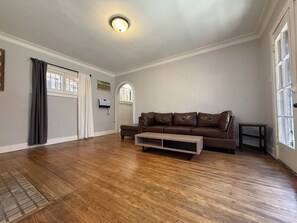 A spacious living room with hardwood flooring, a brown leather sofa, and a ceiling light fixture. - Spacious One Bedroom in Hollywood (Los Angeles)