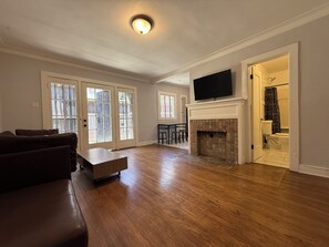 Ein Wohnzimmer mit Holzboden, Kamin, einem darüber montierten Fernseher und einem Essbereich mit Tisch und Stühlen.