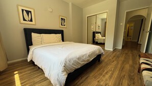 Ein Schlafzimmer mit einem großen Bett, Holzboden und zwei gerahmten Kunstwerken an der Wand.