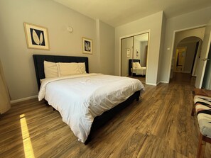 A bedroom with a large bed, wooden flooring, and two framed artworks on the wall. - Spacious One Bedroom in Hollywood (Los Angeles)