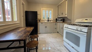 Eine Küche mit einem schwarzen Kühlschrank, weißen Schränken, einem weißen Herd und einem Holztisch mit Hockern.