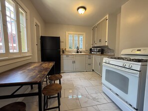 A kitchen with a black refrigerator, white cabinets, a white stove, and a wooden table with stools. - Spacious One Bedroom in Hollywood (Los Angeles)