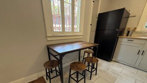 Eine Küche mit einem Holztisch, Hockern, einem schwarzen Kühlschrank und einem Fenster mit dekorativen Sprossen.
