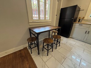 A kitchen with a wooden table and stools, a black refrigerator, and a window with decorative bars. - Spacious One Bedroom in Hollywood (Los Angeles)