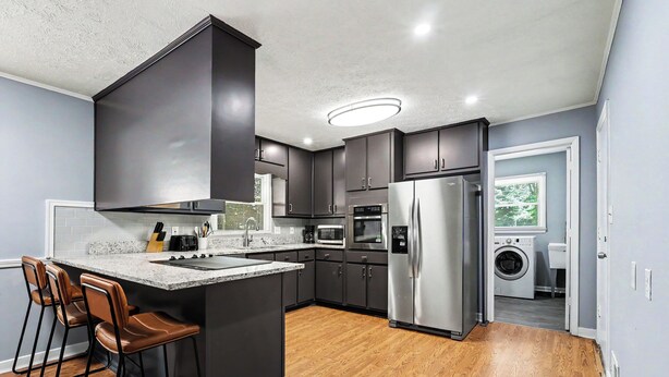 A modern kitchen with dark cabinetry, a central island with bar stools, a stainless steel refrigerator, and a built-in oven. - Luxury Metro Atlanta Retreat - Sleeps 10 (Decatur)