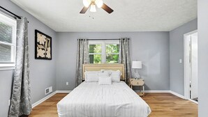 A bedroom with a bed, a ceiling fan, a window with curtains, and a nightstand with a lamp. - Luxury Metro Atlanta Retreat - Sleeps 10 (Decatur)