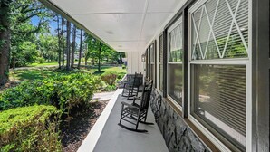 A covered porch with three rocking chairs, a stone wall, and a view of a well-maintained garden and trees. - Luxury Metro Atlanta Retreat - Sleeps 10 (Decatur)