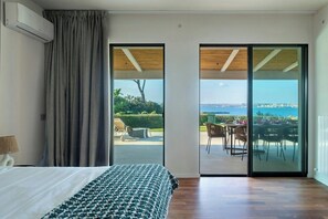 A bedroom with a bed, a bedside lamp, a large window with curtains, and a view of an outdoor dining area with tables and chairs. - House with view of Ortigia and sea access (Siracusa)