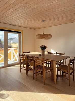 A dining area with a wooden table and chairs, a hanging light fixture, and a view through a glass door. - Yellow beach house with sauna and view over Løkken (Løkken)