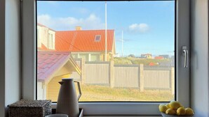 A window with a view of a house, a fence, and a bowl of lemons on the windowsill.