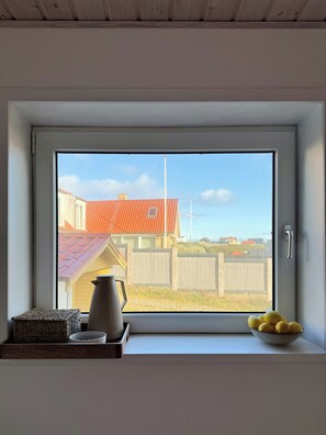 Ikkunasta avautuu näkymä taloon, aitaan ja ikkunalaudalla olevaan sitruunakulhoon.