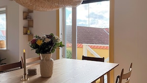 A dining area with a wooden table, chairs, a woven pendant light, and a vase with flowers.