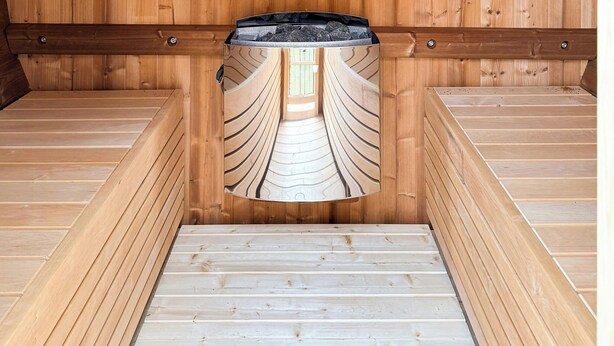A sauna with wooden walls and benches, a central bench with a curved design, and a skylight.