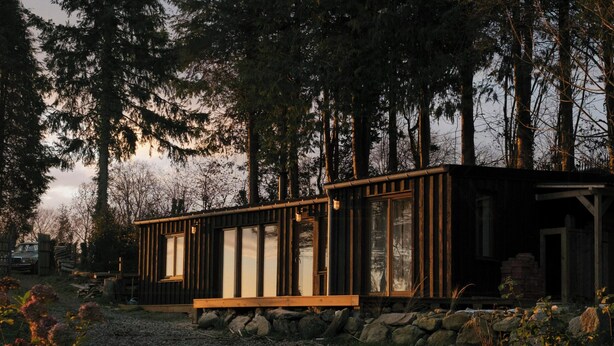 Eine Holzhütte mit einer Holzterrasse, umgeben von dichtem Wald.