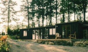 A cabin with a deck, a table, and chairs, surrounded by trees. - Eco-friendly cabin in the Norman countryside (Gathemo)