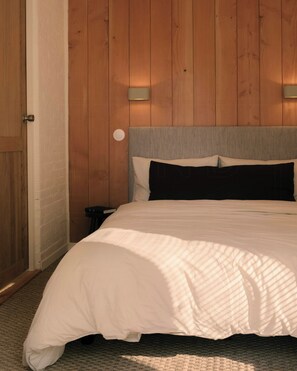 A bedroom with a wooden wall, a bed with white bedding, and two wall-mounted lights. - Eco-friendly cabin in the Norman countryside (Gathemo)