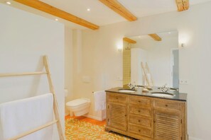A bathroom with wooden beams, a double sink vanity, a toilet, and a patterned floor. - Experience the Uckermark from the old hayloft (Weggun)