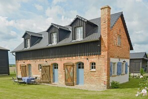 A two-story brick house with a sloped roof, a front porch with a table and chairs, and a small garden area. - Experience the Uckermark from the old hayloft (Weggun)