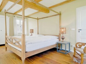A four-poster bed with a wooden frame, a small bedside table with a lamp, and a rocking chair in a room with wooden flooring and a sloped ceiling. - Experience the Uckermark from the old hayloft (Weggun)
