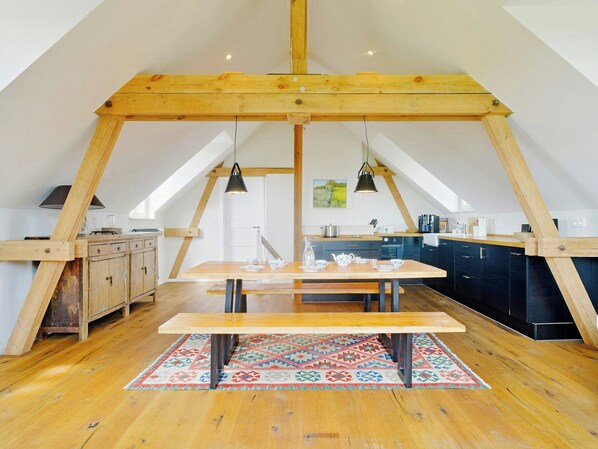 A loft-style kitchen with wooden beams, a wooden dining table, and a colorful rug. - Experience the Uckermark from the old hayloft (Weggun)