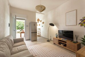 Ein Wohnzimmer mit einer Couch, einem Fernseher, einer Stehlampe, einem Kühlschrank und einem Essbereich mit Tisch und Stühlen.