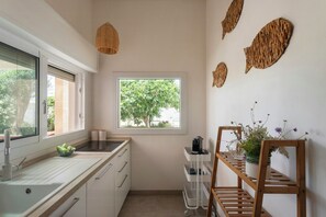 Eine Küche mit Fenster, Spüle, einem Holzregal mit Pflanzen und einem Wandregal.