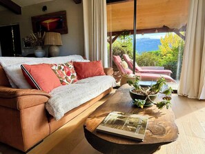 Un salon chaleureux avec un canapé, une table basse sur laquelle repose un livre, et une vue sur un balcon aménagé avec du mobilier d’extérieur.