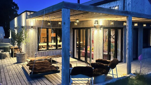 An outdoor covered patio area with wooden flooring, a pool, and seating arrangements. - Nordic architecture with room for the whole family (Odder)