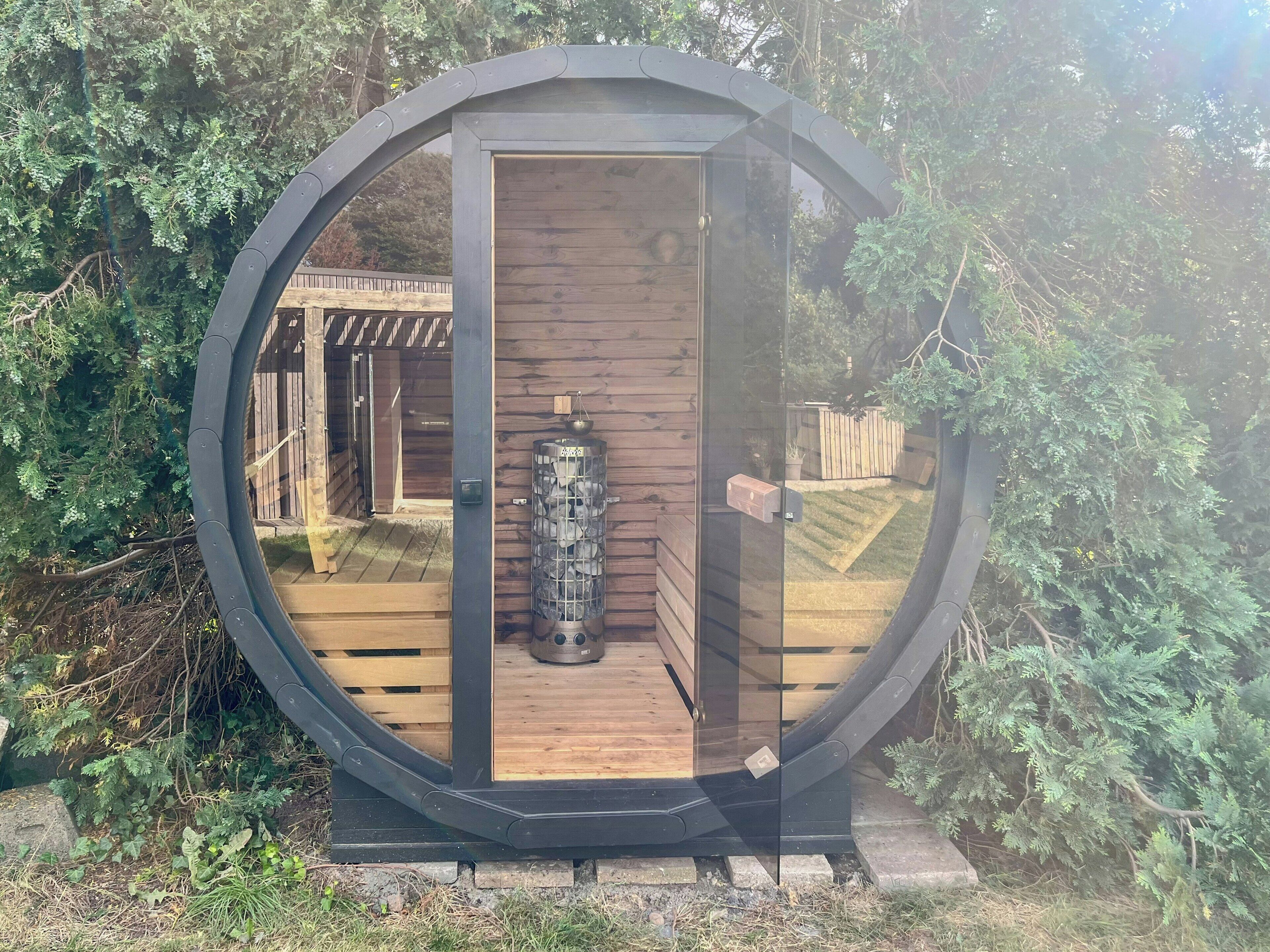 Une structure circulaire en bois, dotée d’une porte en verre, d’un radiateur en métal et d’une terrasse en bois.