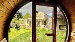 A circular window with a view of a wooden house, a hammock, and a fenced yard. - Nordic architecture with room for the whole family (Odder)