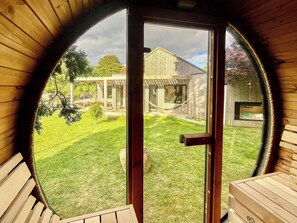 Ein rundes Fenster mit Blick auf ein Holzhaus, eine Hängematte und einen umzäunten Garten.