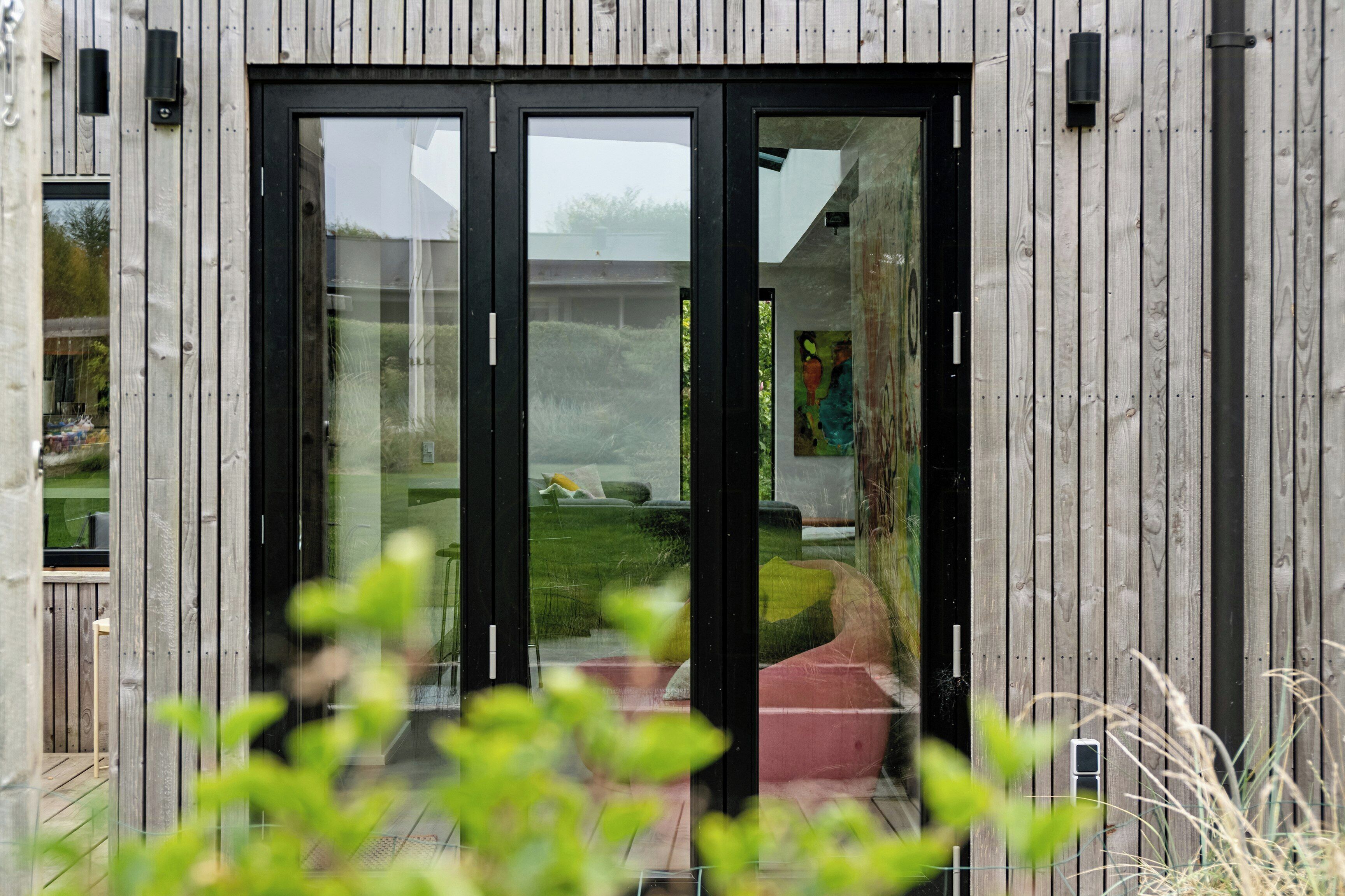 A modern building with a wooden exterior, large glass doors, and a visible outdoor seating area.