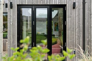 Ein modernes Gebäude mit Holzfassade, großen Glasüren und einem sichtbaren Außenbereich mit Sitzgelegenheiten.