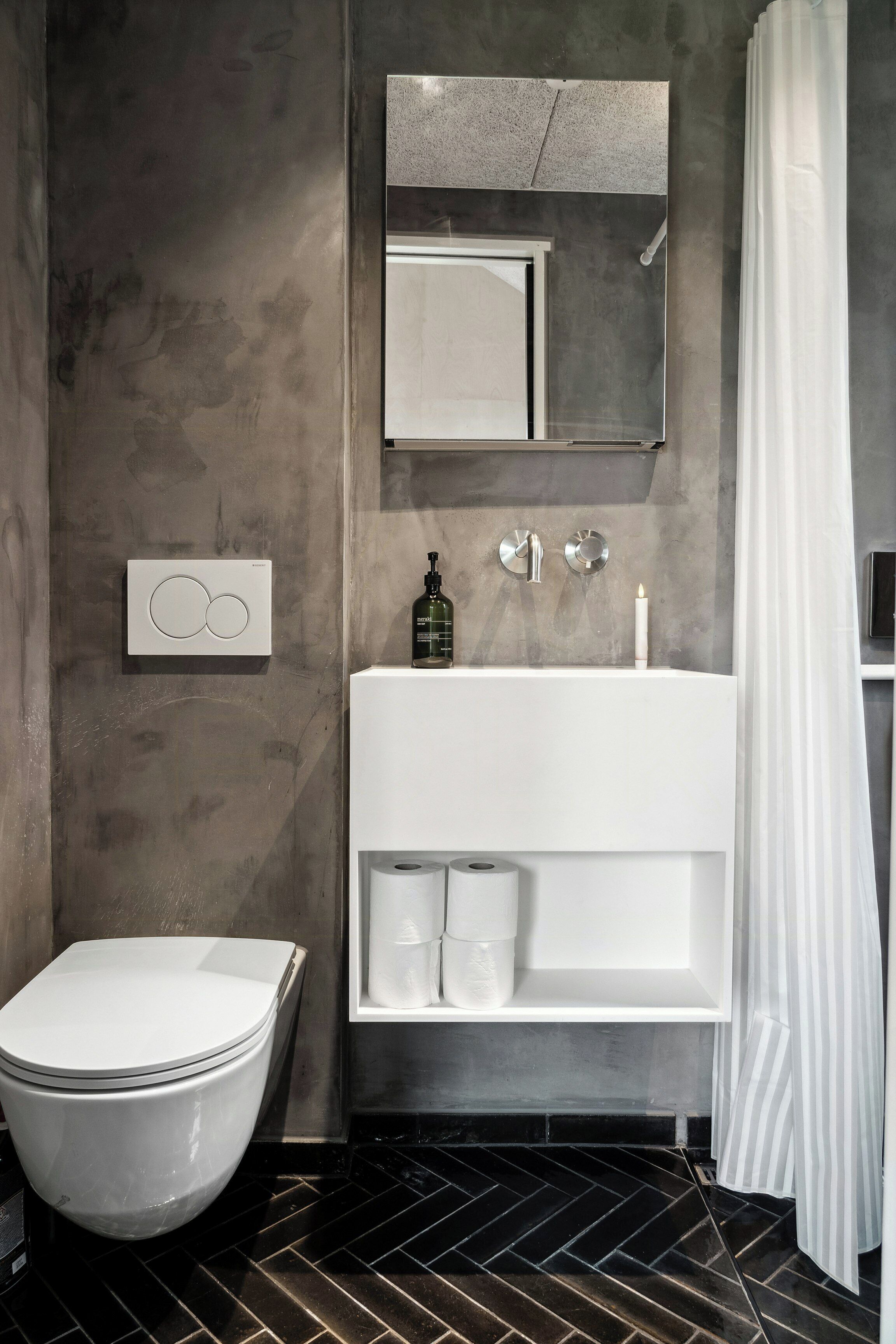 A modern bathroom with a toilet, a large mirror, a white sink, and a shower curtain.